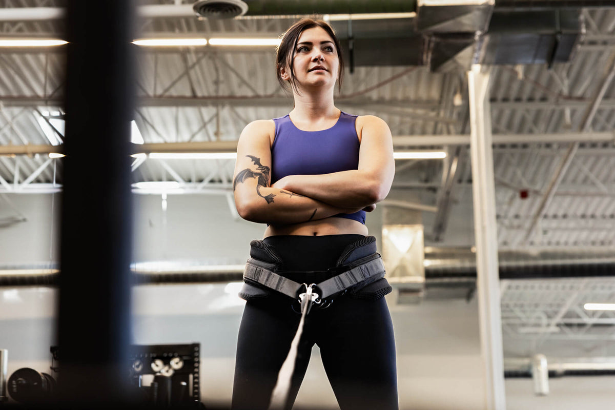 An athlete stands with her arms crossed and a belt squat belt around her hips.