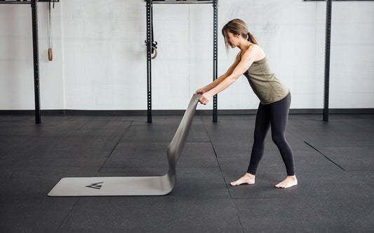 A woman places a yoga mat on the ground, preparing to cool down.