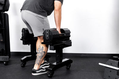 Athlete picking up REP® x PÉPIN™ adjustable dumbbells from a metallic black REP® Adjustable Dumbbell Stand