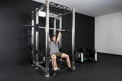 An athlete doing barbell shoulder presses with the Colorado barbell and old school iron weight plates