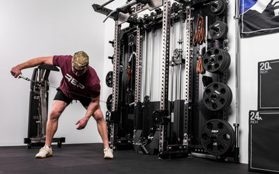 An athlete using the REP® x Kleva Built® ISO Pushdown Grip Cable Attachment to perform bent over tricep kickbacks
