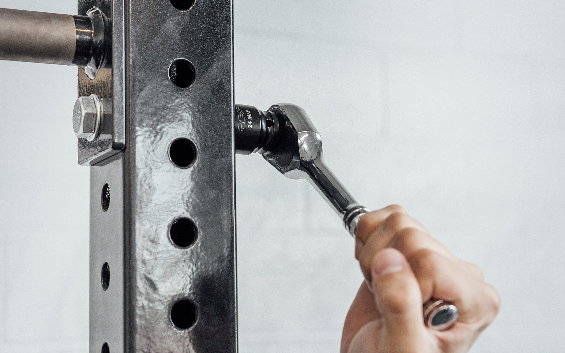 Someone using a ratchet wrench with REP's 24mm Rack Socket to install a bolt on a 4000 Series Power Rack
