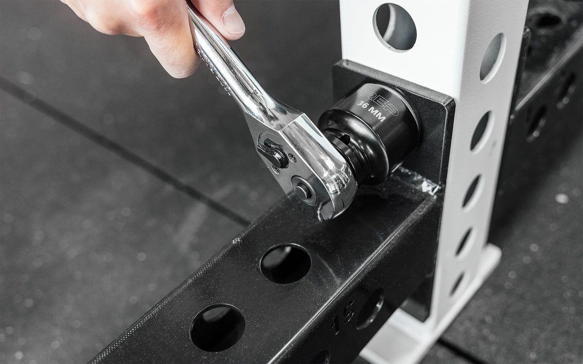 Someone using a ratchet wrench with REP's 36mm Rack Socket to install a bolt on a 5000 Series Power Rack