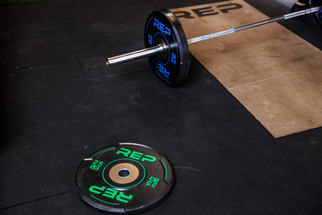 High-angle: Barbell with 45 lb REP Sport Bumper Plates 2.0 on platform; 25 lb plate on floor nearby