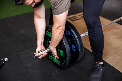 High-angle: Athlete adds a 25 lb REP Sport Bumper Plate 2.0 to a barbell already loaded with a 45 lb plate
