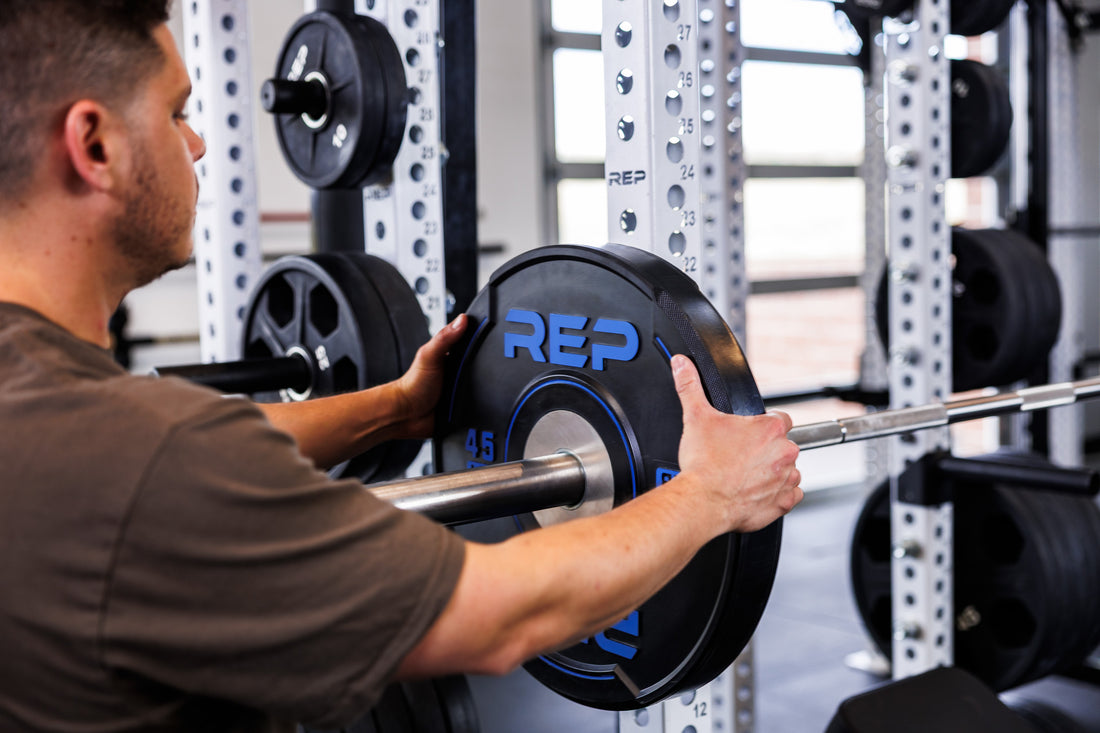 Action-shot: Athlete loading a barbell with a 45 lb REP Sport Plate 2.0 while racked on the front of a PR-5000 Power Rack