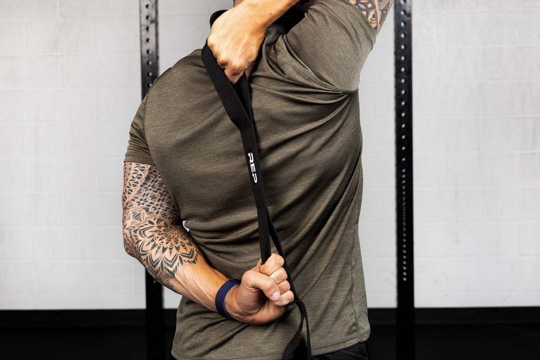 Person wearing a green athletic shirt using stretching band in a gym setting
