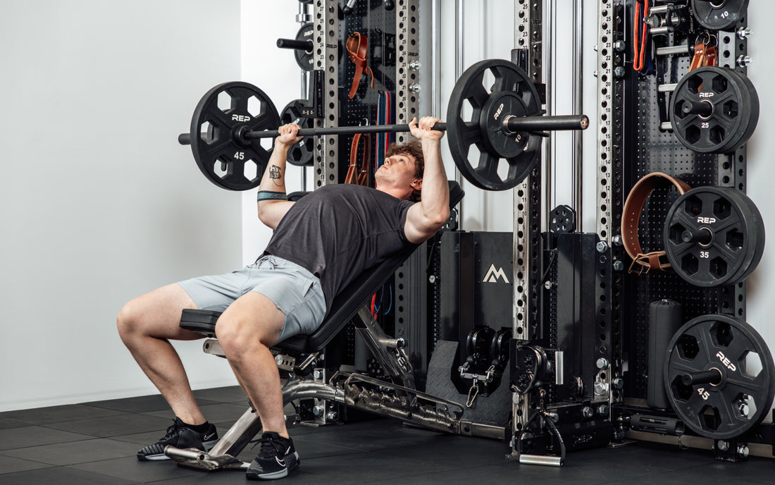 An athlete incline bench pressing off the front of the Wall-Mounted Ares™ 2.0 while laying on a REP BlackWing™ bench